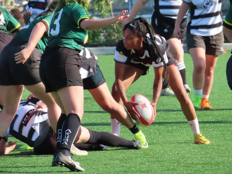 A Women's+ Lions player reaches to ground the ball against a side in green