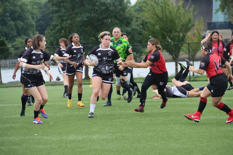 A Women's+ Lions player carries the ball as a tackle goes in behind her
