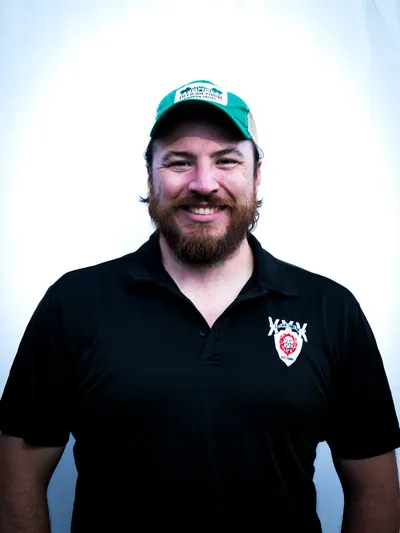 James Johnston, smiling, in a green cap and a black Village Lions polo shirt