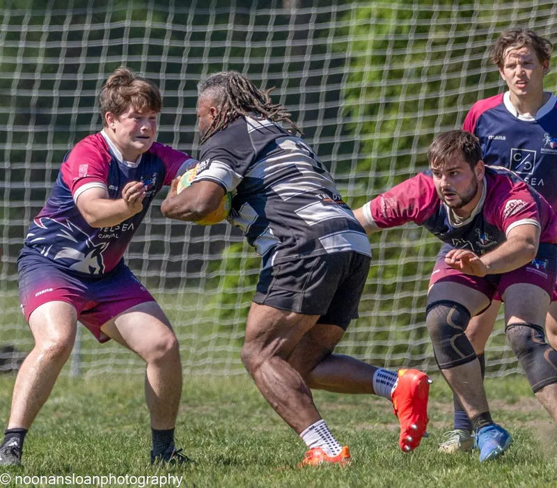 A Lions ball carrier runs straight at two defenders in maroon in front of the posts